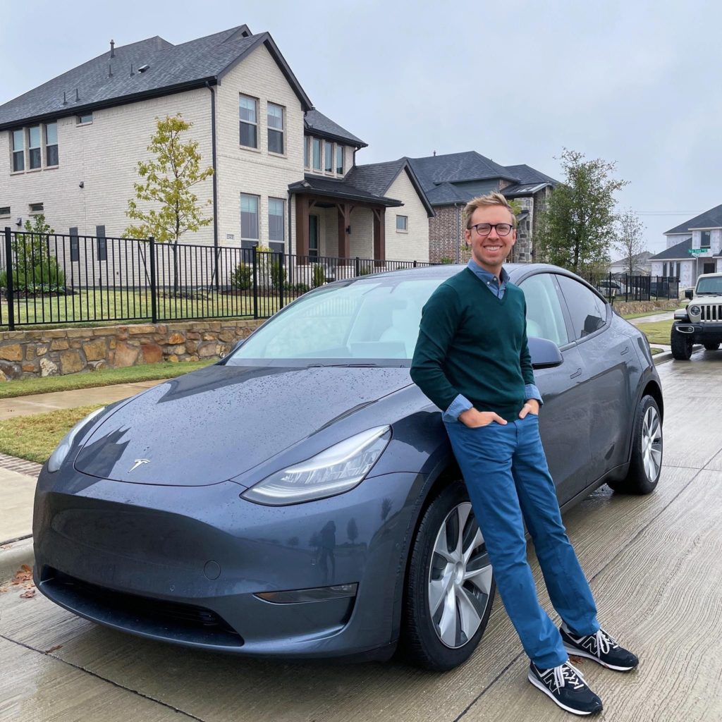 attractive man standing in front of a Tesla Model Y in Frisco, Texas