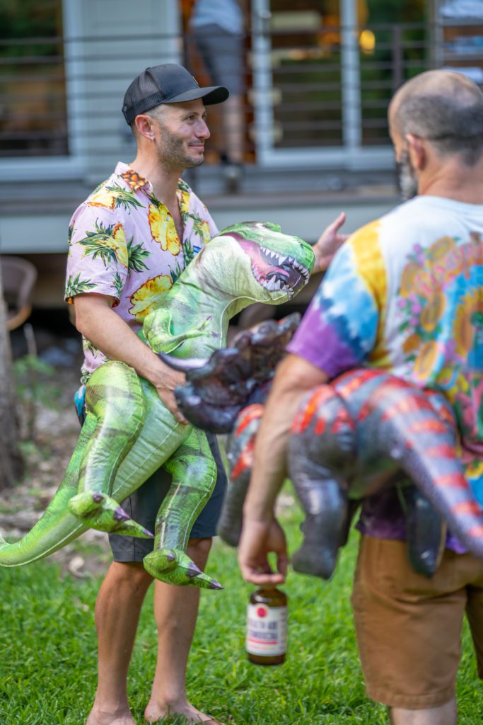 American man (Noah Kagan) holding an inflatable T-Rex outside at a party