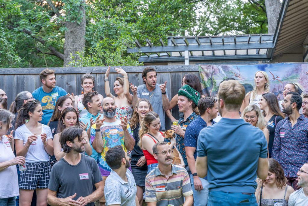 Group of adults gathering for a group photo outside with dinosaur poster behind them