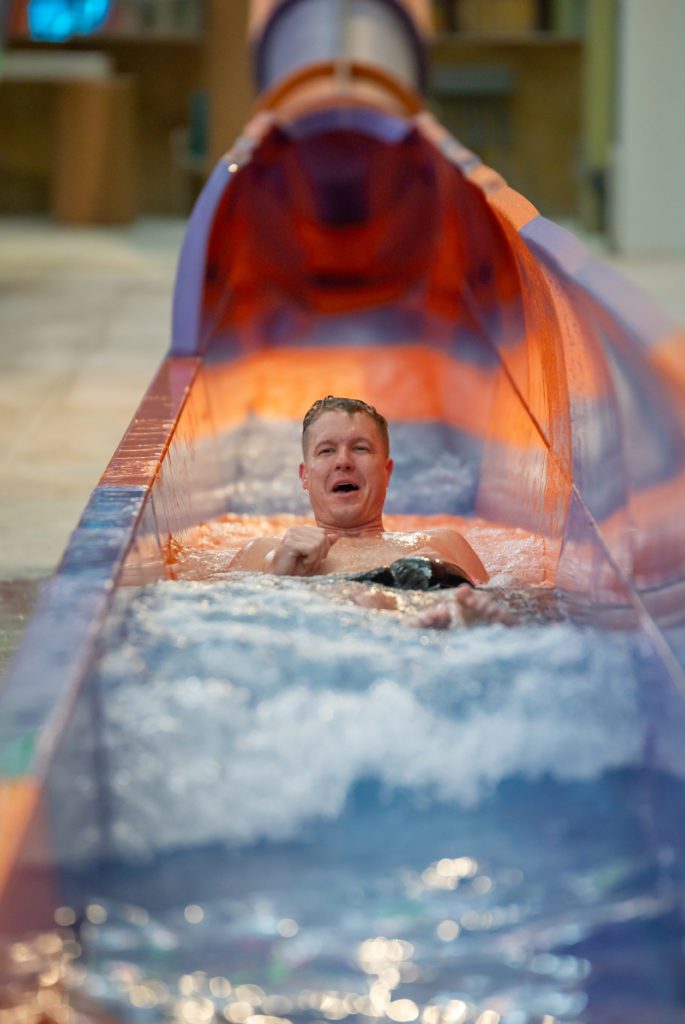 Sam Parr riding down a steep water slide, at the end of the slide here