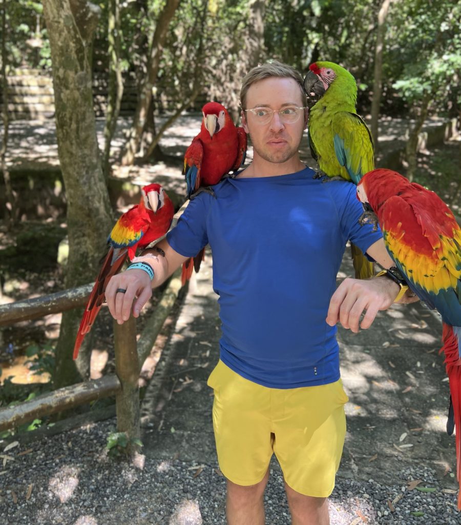 man with many macaw parrot birds on his arms and shoulders