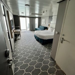 door opens into a balcony room on a cruise ship showing bed and carpets
