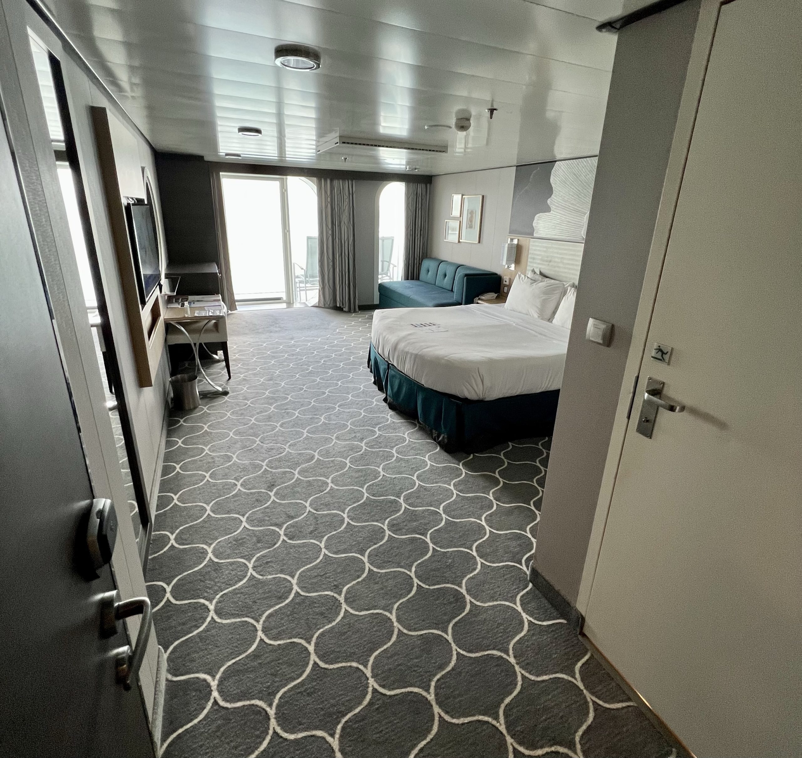 door opens into a balcony room on a cruise ship showing bed and carpets