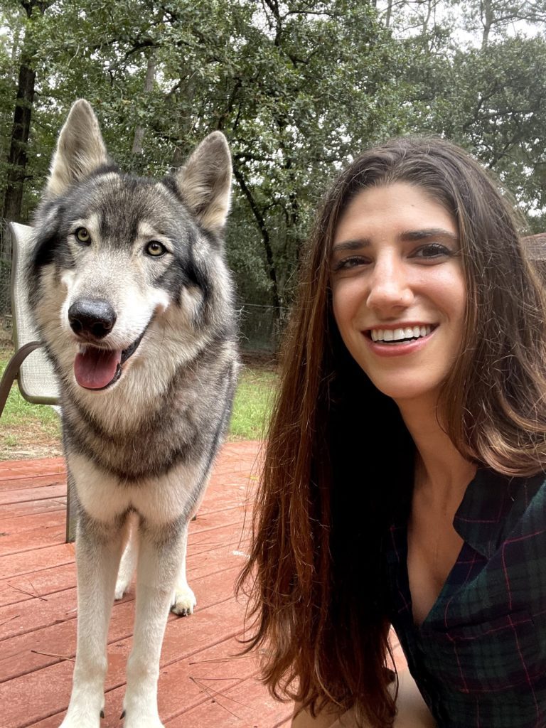 a woman smiling for the camera with a wolfdog